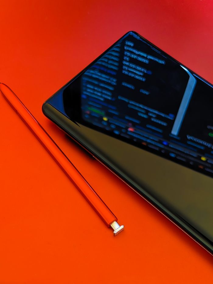 Close-up of a smartphone with a stylus on a bright red surface, showcasing modern technology.